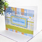 A handmade greeting card with a blue and yellow patterned design, featuring the text 'Hugs & Kisses' on a blue label, set against a white background with a green plant leaf in the corner.